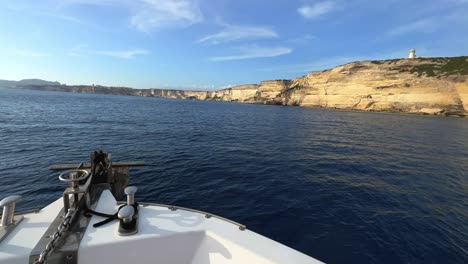 point of view of sailboat bow navigating toward corsica island cliffs and capo pertusato lighthouse in france, 50fps