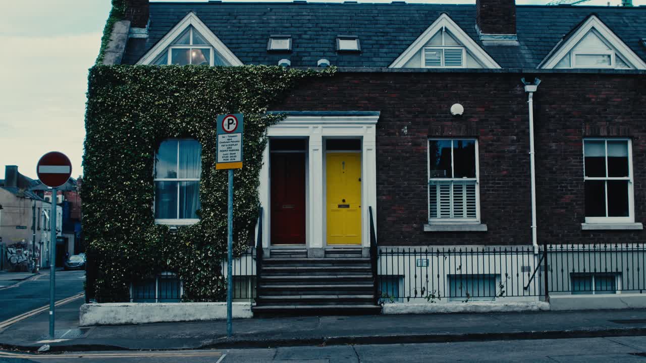 Static shot of brick row houses with colorful doors, ivy, and street signs in soft urban light - Ireland