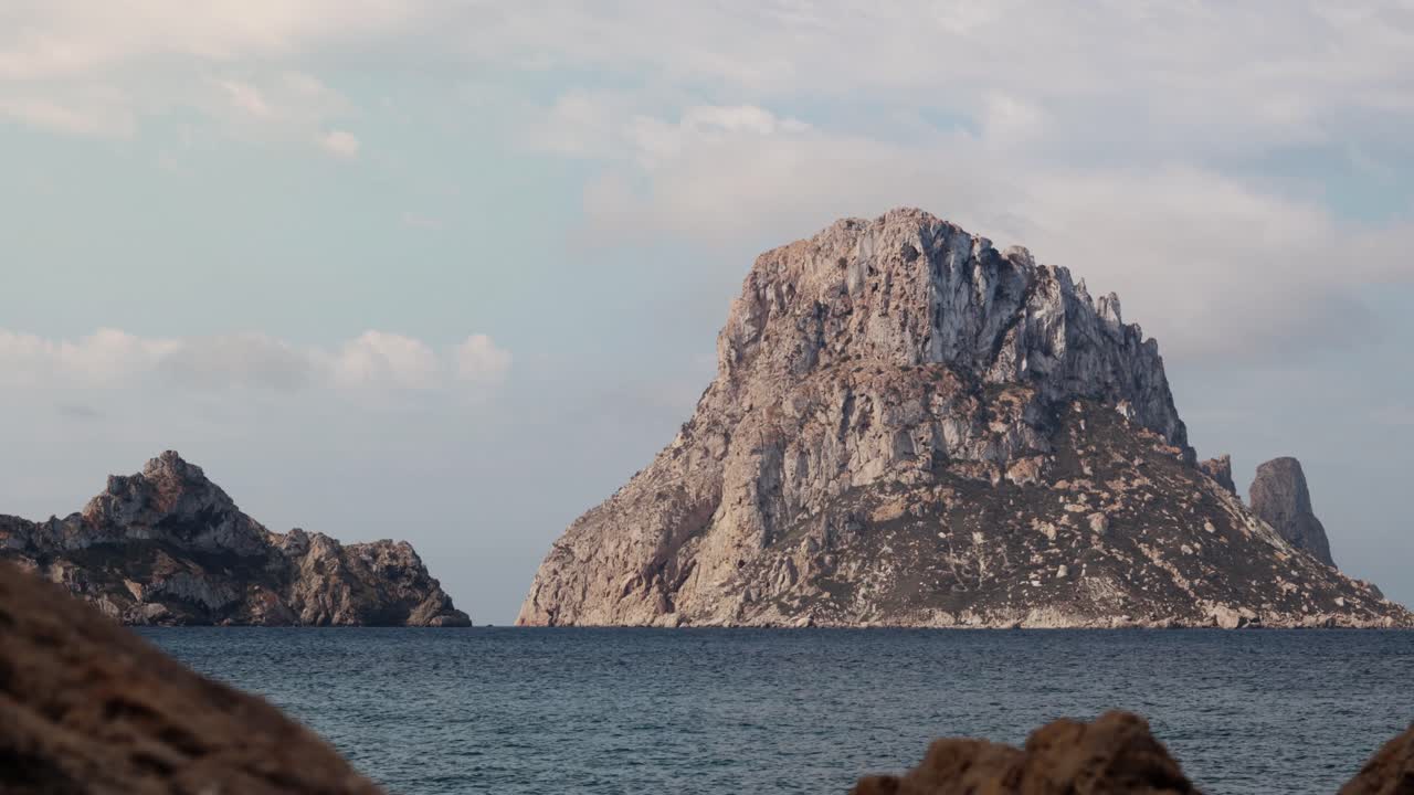Timelapse statico di Es Vedra a Ibiza con nuvole che si muovono velocemente e barche che attraversano le acque turchesi del Mediterraneo.