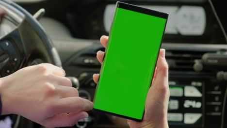 la mano de la mujer del conductor en el coche utiliza un teléfono inteligente con una pantalla verde, dentro de un coche. versión 2