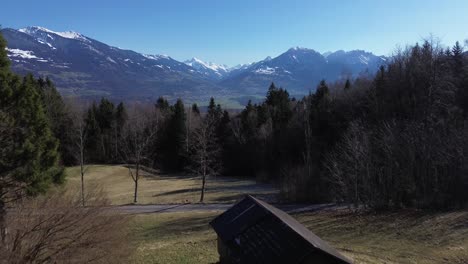 Drohnenflug-Vorbei-An-Kleiner-Berghütte-Im-Kiefernwald-Mit-Malerischer-Aussicht-über-Schneebedeckte-Berglandschaft,-Vorarlberg,-Österreich