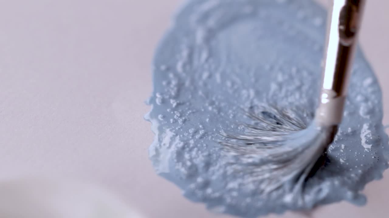 Extreme close-up of a brush mixing textured light blue paint on a white artist palette