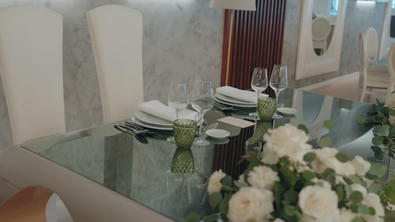 Glass dining table prepared with plates wine glasses cutlery and white floral centerpiece in refined interior