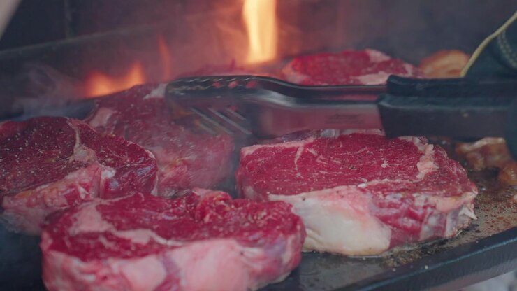 Kebab, steak, dan sosis mendesis di atas piring BBQ panas selama acara masak-masak luar ruangan yang menyenangkan, menampilkan makanan segar, rasa berasap, dan santapan musim panas yang santai