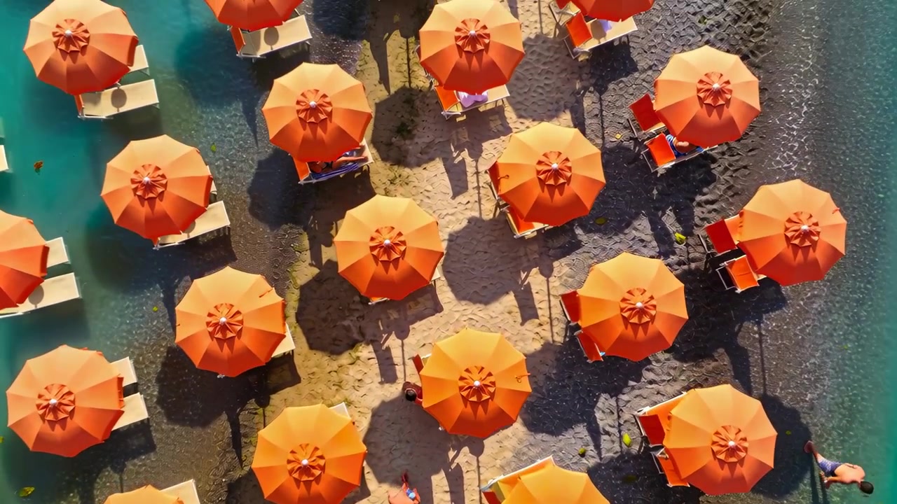 Mostra ombrelloni arancioni su una spiaggia di ciottoli, una persona in costume da bagno a destra in piedi, che si tuffa per nuotare.