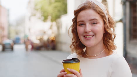 happy redhead young smiling woman relaxing enjoying morning coffee hot drink outdoors city street
