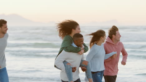 group of friends having fun running along winter beach together