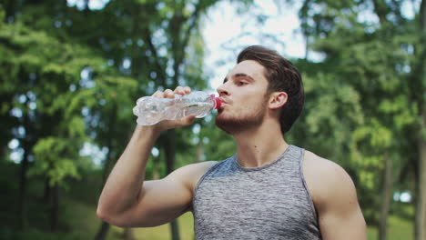 hombre de fitness bebiendo agua mineral después de hacer ejercicio entrenando al aire libre