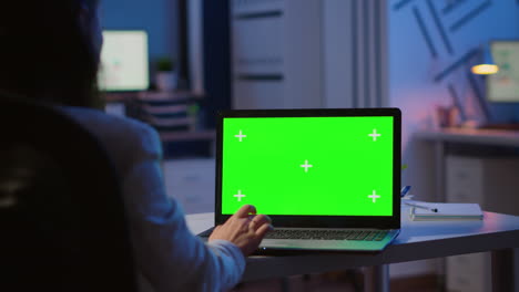 mujer mirando una computadora portátil con una maqueta verde durante la noche