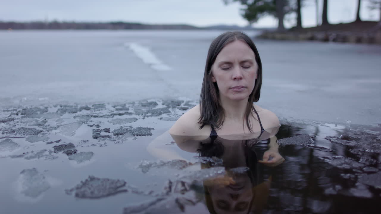 얼음에서 목욕하는 여성이 손을 합쳐서 조용히 숨을 쉬고 슬라이더를 습니다.