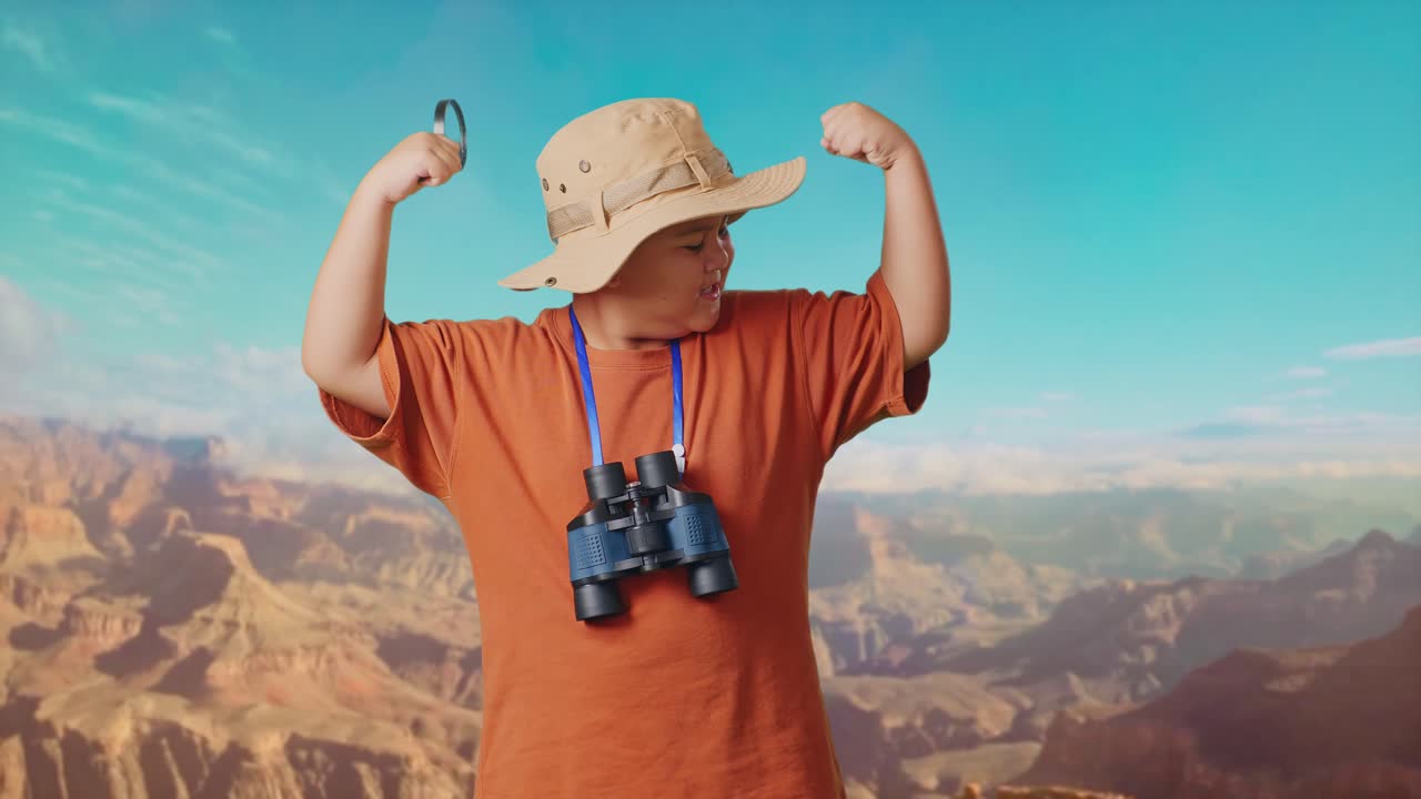 Asian Boy With A Hat And Binoculars Using The Magnifying Glass Then Flexing His Bicep While Traveling At The Top Of Mountain. Boy Researcher Examines Something, Travel Tourism Adventure Concept