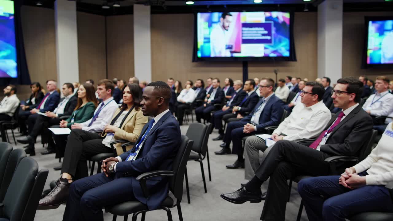 A corporate seminar with attendees seated in rows, viewed from a side angle