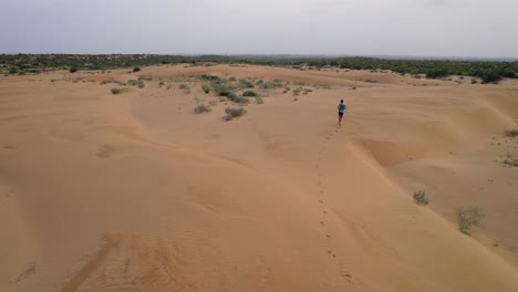 Vista-Aérea-Escénica-De-Drones-Rastreando-A-Un-Joven-Corriendo-A-Través-De-Las-Dunas-En-El-Desierto