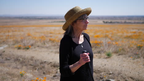 A-happy-middle-aged-woman-with-gray-hair-walking-in-a-field-of-flowers-on-a-hike-with-her-walking-stick-SLOW-MOTION