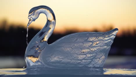 a beautifully crafted ice sculpture of a swan with water dripping from its beak against a stunning sunset background, showcasing artistic skill and nature's beauty