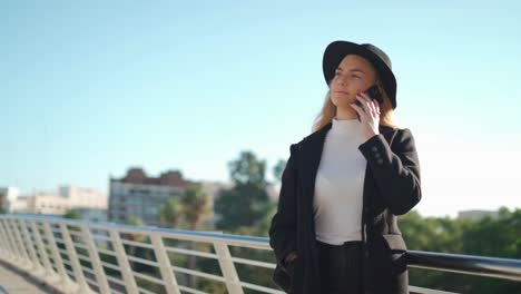 young woman talking on mobile phone on bridge in sunlight