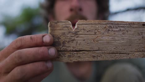 Caucasian-male-survivalist-inspecting-notch-in-fireboard-at-camp-in-wilderness