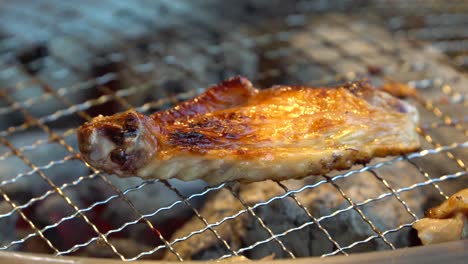 turning marinated chicken wing with tong on korean barbecue, close up