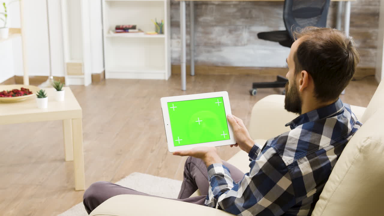 Man using a tablet with a green screen at home