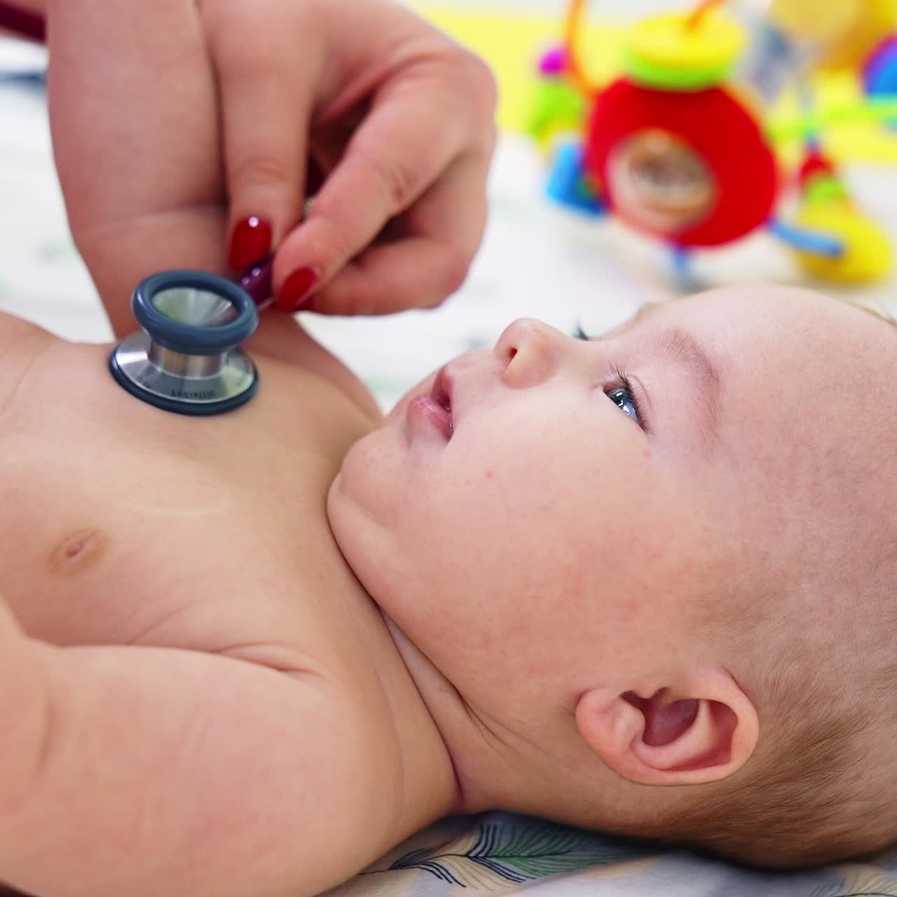 Pediatrician hand puts stethoscope on child's chest. Baby looks interested and smiles to the doctor. Blurred backdrop