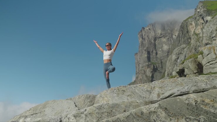 Donna esegue la posizione dell'albero yoga su una costa rocciosa, vista frontale al rallentatore