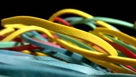 macro toma de bandas elásticas de colores de papelería sobre fondo negro. concepto de suministros para el hogar, la oficina, el banco, la farmacia, el correo. zoom out.