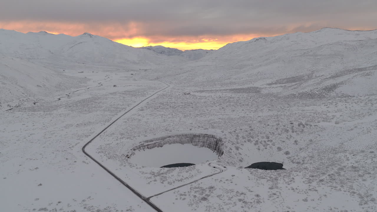 Le doline gemelle Pozo de las Ánimas a Malargüe, Mendoza, Argentina, situate in un altopiano vulcanico coperto di neve con strada e le Ande distanti che brillano all'alba, ripresa fluida con drone in allontanamento
