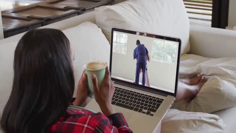 Compuesto-De-Mujer-Sentada-En-Casa-Sosteniendo-Un-Café-Viendo-Un-Partido-De-Judo-En-Una-Computadora-Portátil