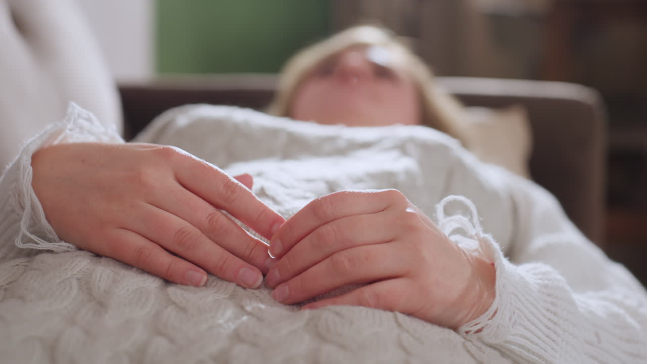 Peace seeker lying on cozy sofa draped in knit sweater with hands crossed over soft blanket, eyes closed, breathing calmly during therapy session, gentle lighting highlights relaxed posture