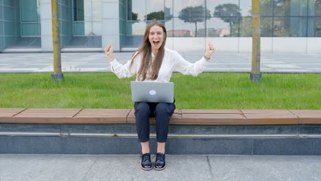 una joven feliz y emocionada sentada con una computadora portátil, celebrando en cámara lenta