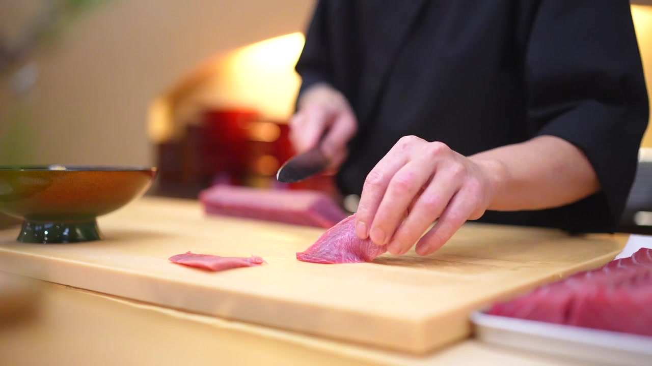 Profesjonalny szef kuchni przygotowujący surową rybę na drewnianej desce do krojenia w tradycyjnej japońskiej restauracji.