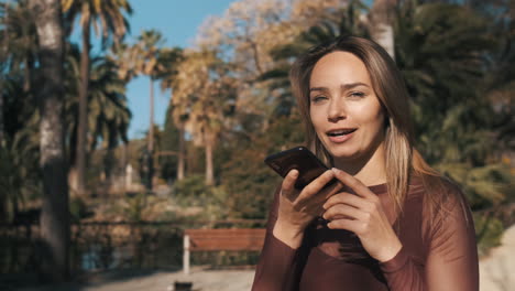 mujer de ojos azules sonriendo usando mensajero de voz al aire libre.