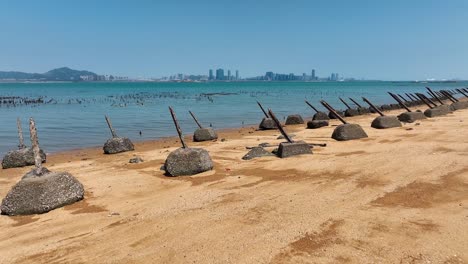 Aerial-ascending-shot-of-sandy-beach-with-anti-landing-barrier-on-Kinmen-金門-island-with-chinese-skyline-in-Background---Scare-of-war-against-China