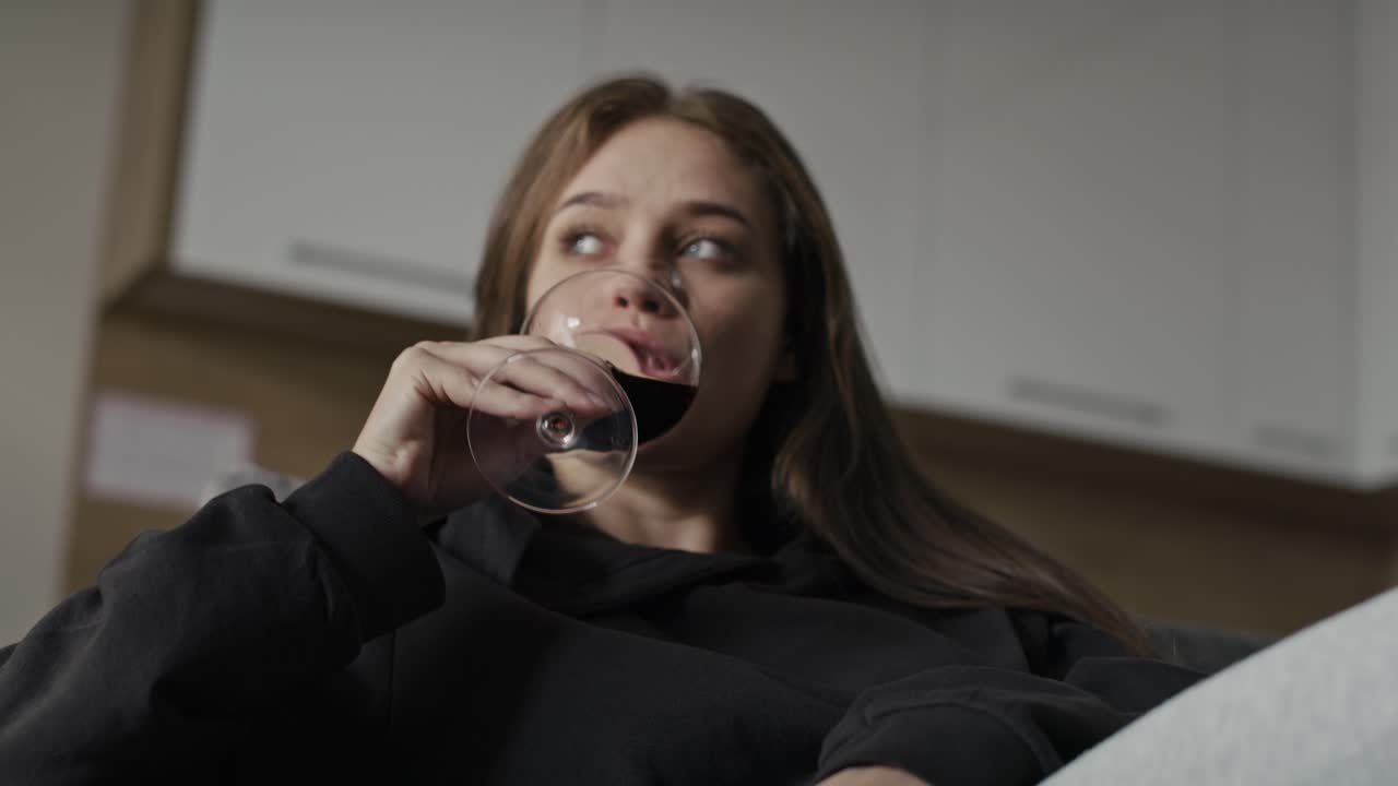 Sad caucasian woman with problems drinking red wine at home.