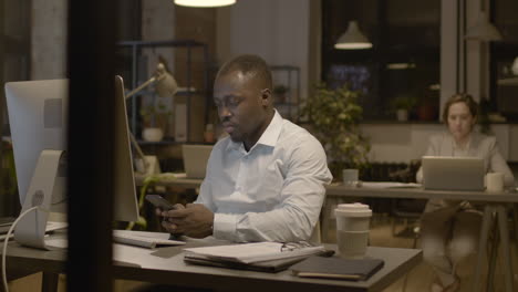 american man texting on smartphone and woman employee working on computer in the office