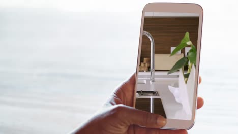 persona que sostiene un teléfono inteligente con interiores de cocina modernos mostrados en la pantalla