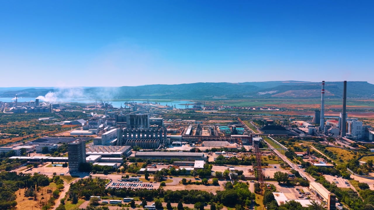 Endüstriyel tesisin panoramik havadan görünümü. Büyük fabrika kompleksi, mavi gökyüzü altında dağların yakınındaki manzaraya yayılıyor.