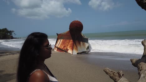 Ein-Model,-Das-Den-Blick-Auf-Den-Strand-Genießt,-Mit-Einem-Schiffswrack-Im-Hintergrund