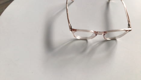 Modern-eyeglasses-in-light-colour-lie-on-a-white-table,-bright-glasses-frame,-slow-motion-footage