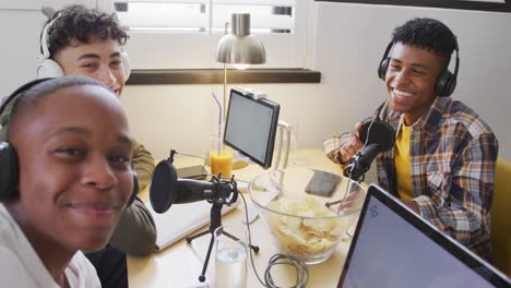 portrait of happy diverse male teenage friends using laptop and recording podcast, slow motion