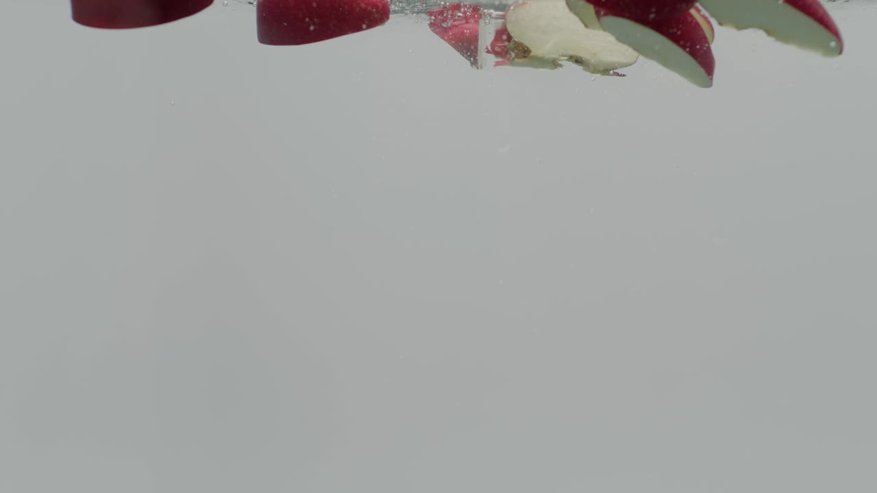 cámara lenta roja de deliciosas rebanadas de manzana cayendo en el agua