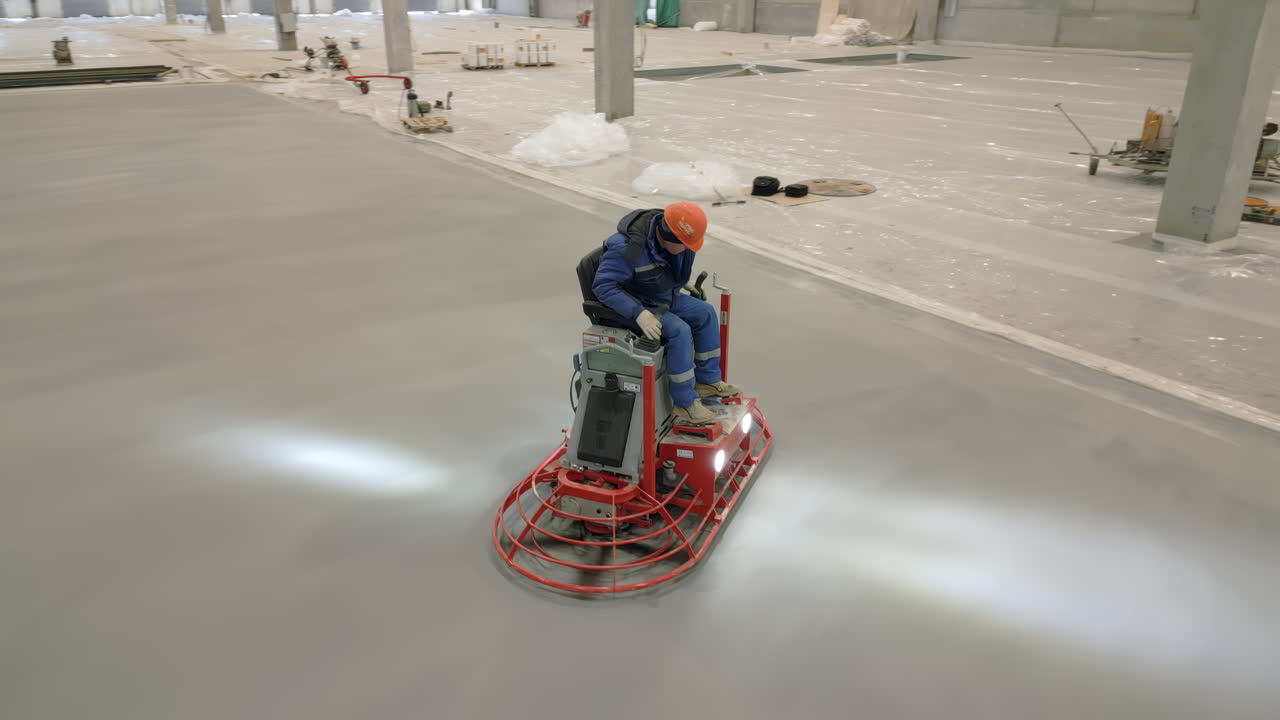창고 의 콘크리트 바닥 을 마무리 하기 위해 전력 트로웰 을 사용 하는 노동자