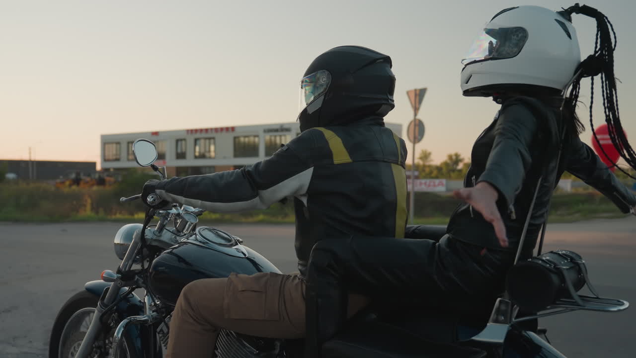 Motorcycle rider in helmet and leather jacket drives on road carrying passenger who spreads hand with joy, showing sense of freedom, motion, lifestyle, and adventure against urban