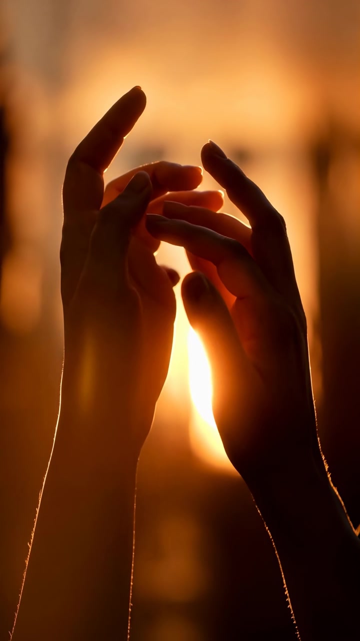Primo piano di due mani che si alzano e si separano delicatamente mentre la calda luce del sole splende attraverso le dita, creando un bagliore solare luminoso, una morbida foschia dorata, una silhouette illuminata dal bordo, un'atmosfera calma e speranzosa e una sensazione di benessere luminoso.