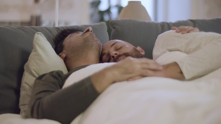 Homoseksuelle mænd krammer hinanden, mens de sover i sengen om morgenen.