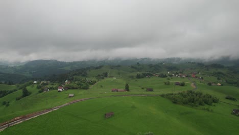 Overcast-sky-hovers-above-a-serene-village-nestled-among-green-hills,-giving-a-tranquil-rural-feel,-aerial-view