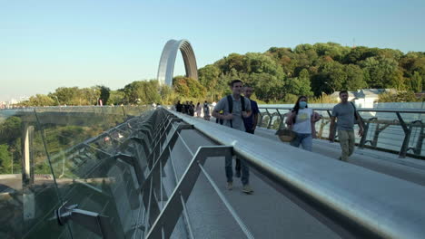 wide dramatic shot of people walk across the glass bridge in kiev on a warm autumn evening.