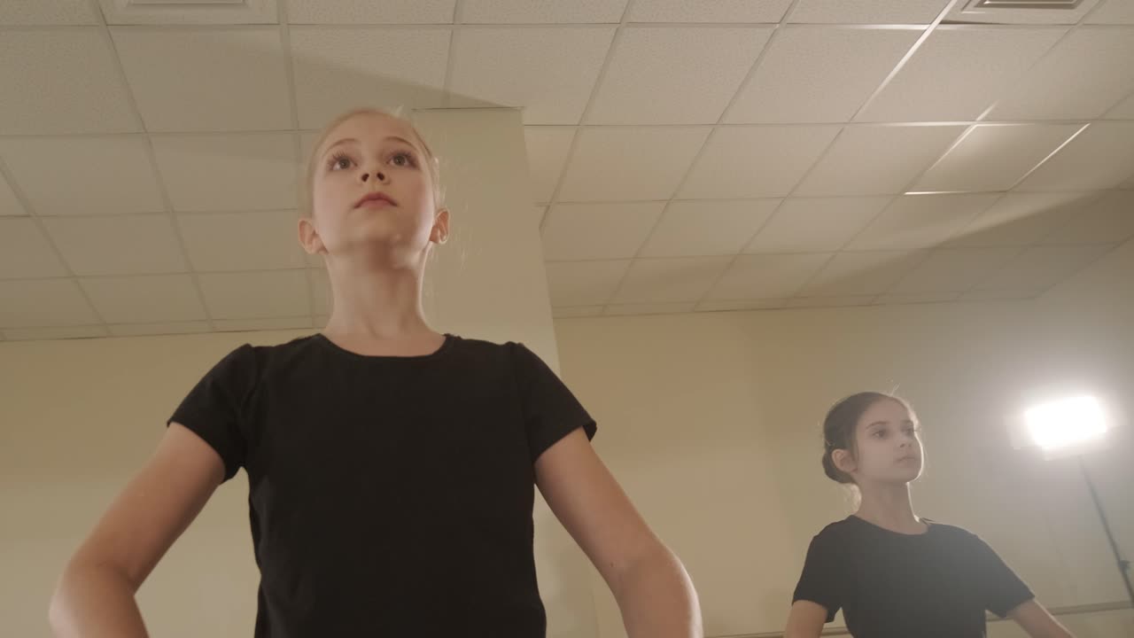 un grupo de jóvenes estudiantes de ballet con ropa de baile negra practicando posiciones en un amplio estudio de ballet con pisos de madera y barras montadas en la pared. expresiones enfocadas y movimientos sincronizados.