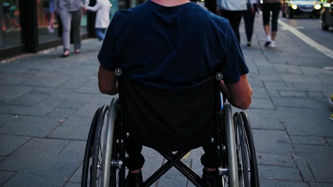 Street-level video shot from behind a person in a wheelchair, capturing urban life and movement