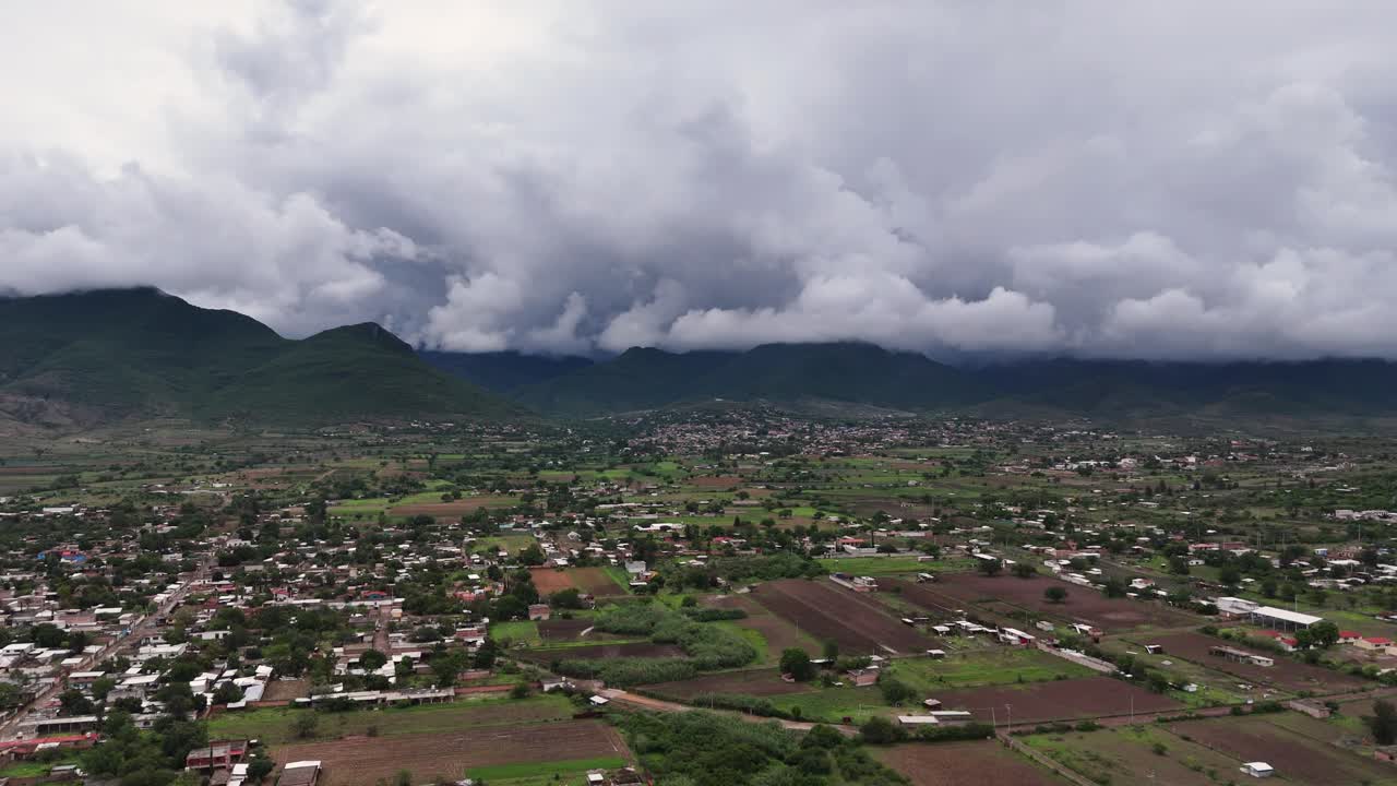Aerial View of Rural Town and Farmland with Mountains Under Cloudy Sky